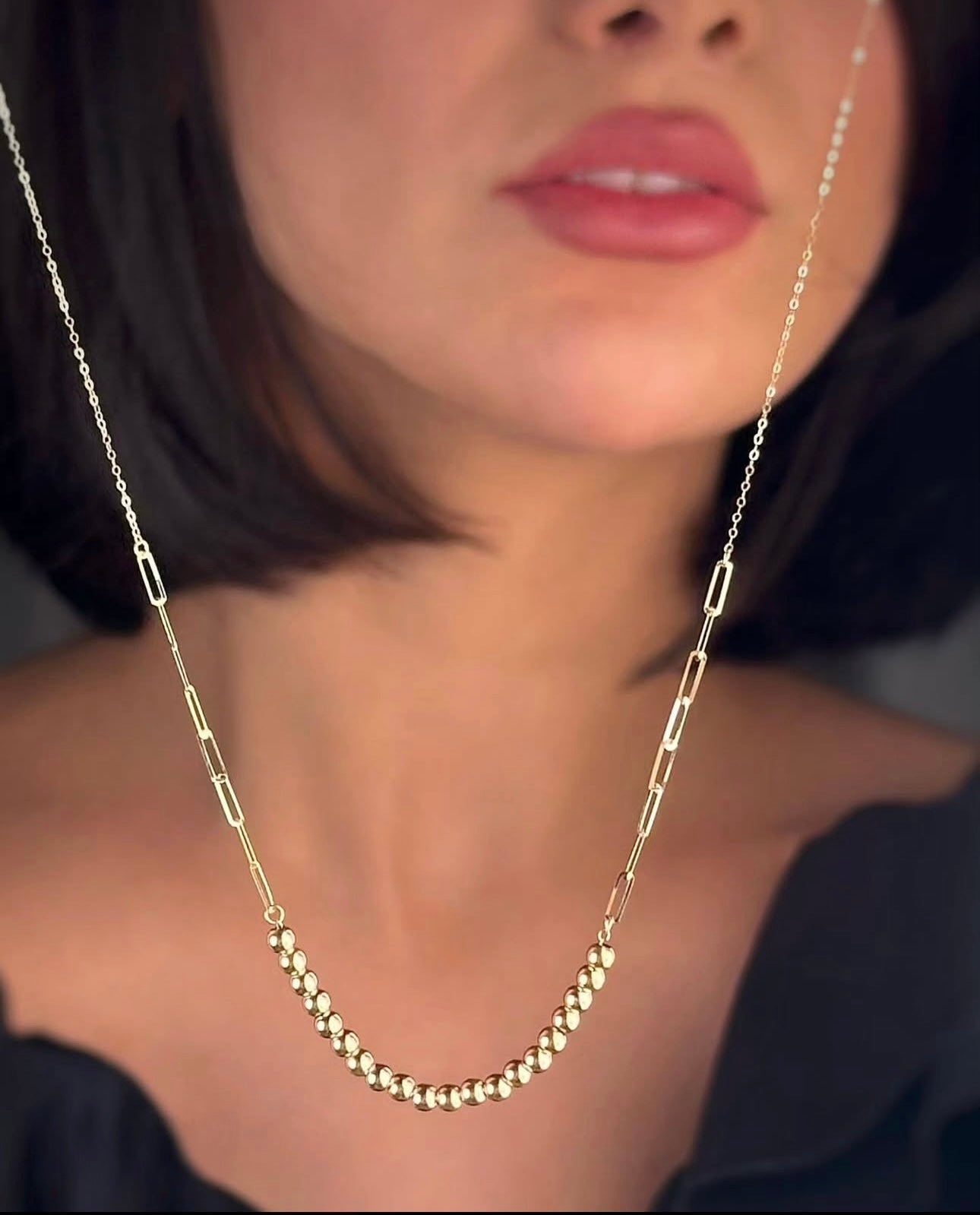 Zanjir Tala-e Morvarid im Vordergrund inszeniert – Goldperlenkette hängt frei vor dem Model, stilvoll präsentiert mit Fokus auf Glanz und Struktur