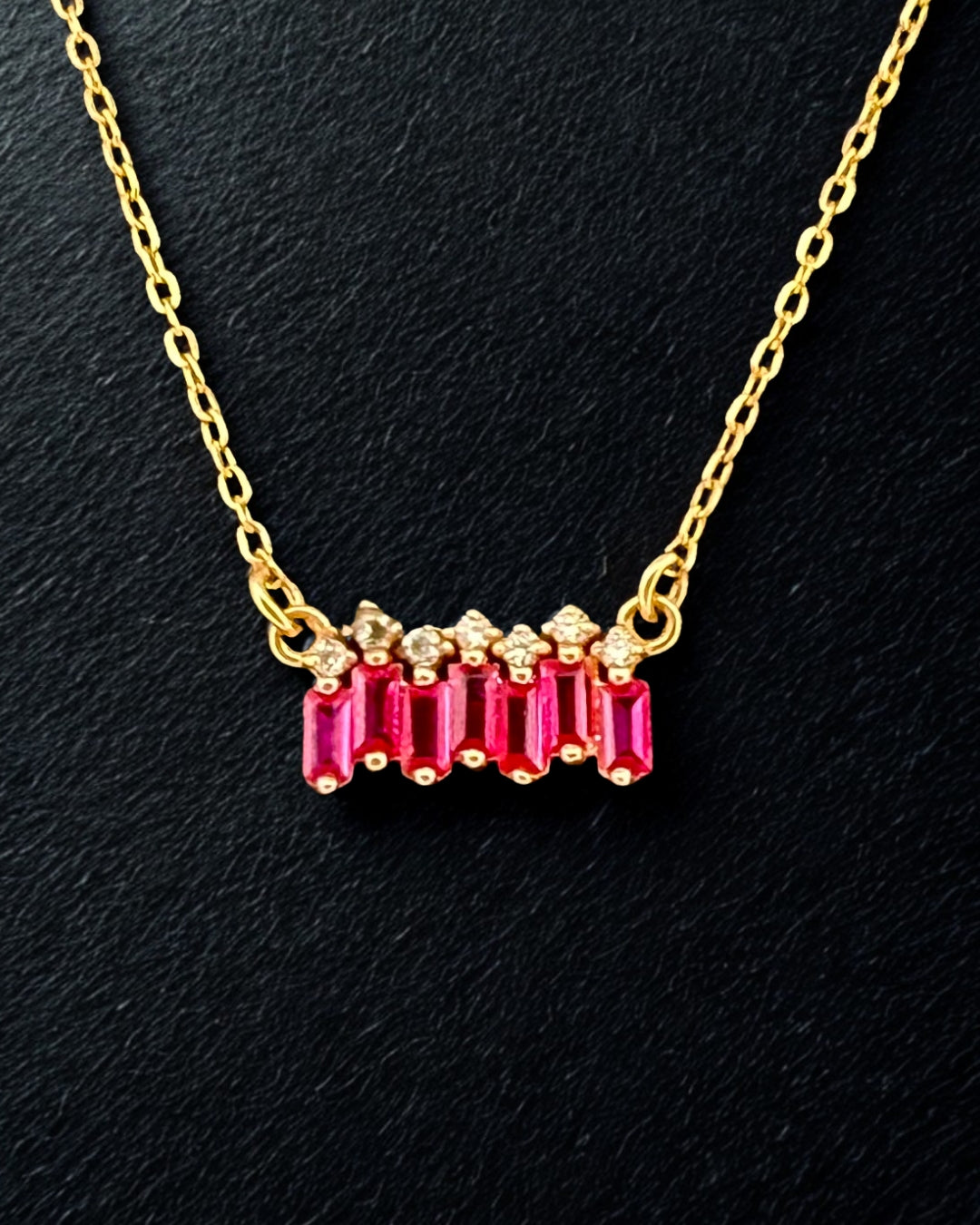 18k-Goldkette mit rubinroten Baguette-Zirkonia auf dunklem Untergrund – feine Ankerkette, zentraler Queranhänger.