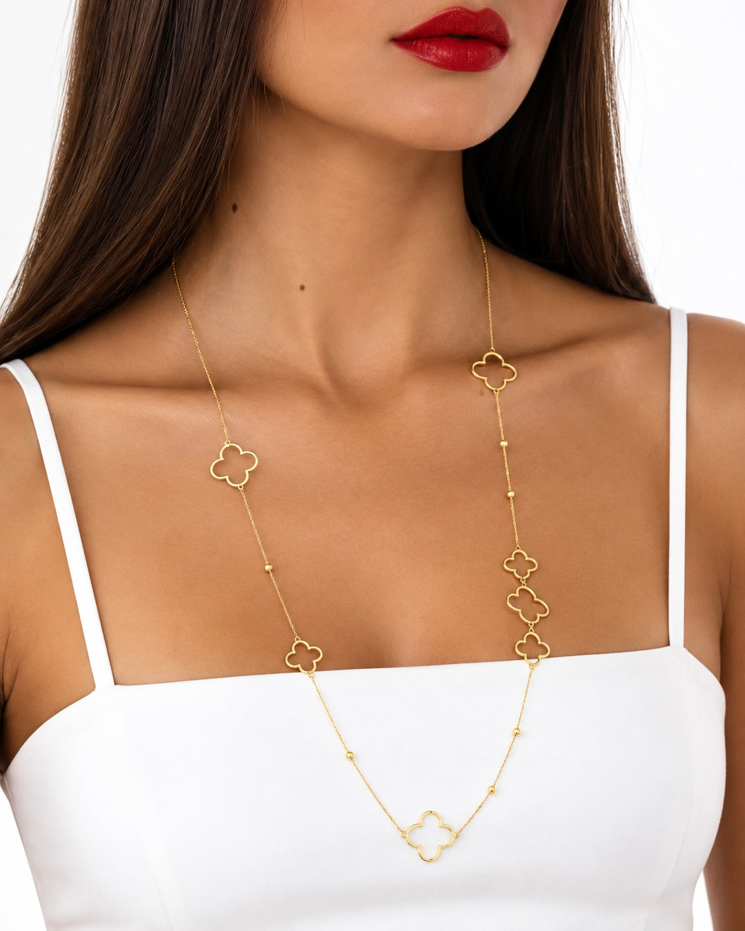 Frau mit langer, filigraner Goldkette mit mehreren vierblättrigen Kleeblatt-Motiven aus 18 Karat Gold, kombiniert mit einem weissen Top.