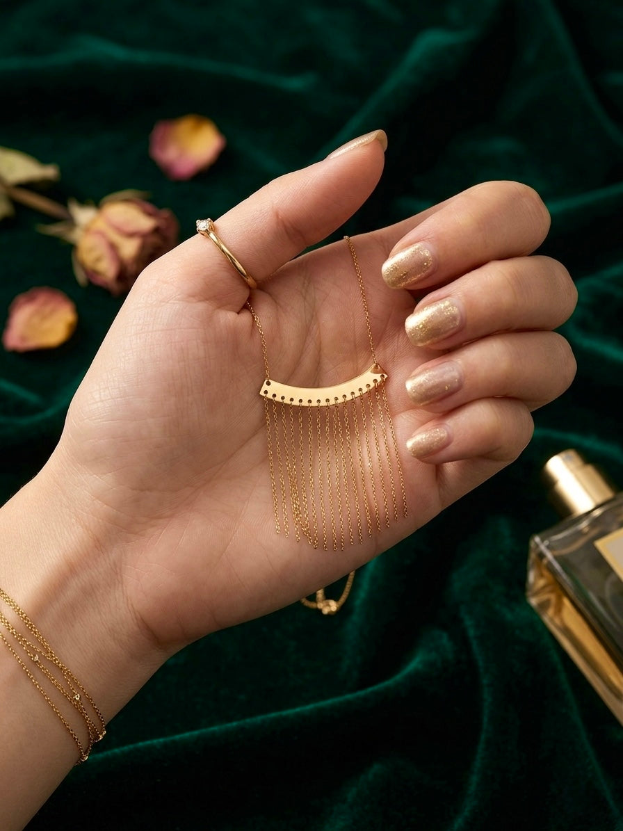 Handgefertigte Halskette aus 18 Karat Gelbgold mit feinen Kettenfransen, elegant präsentiert auf einer Hand vor dunkelgrünem Samt.