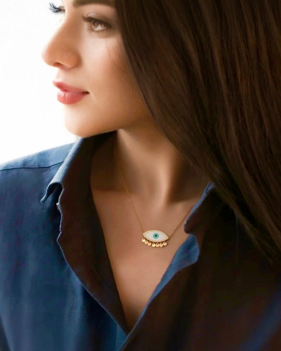 Modell trägt eine filigrane Halskette aus 18k Gelbgold mit Schutzauge-Anhänger, elegante Nahaufnahme am Hals vor hellem Hintergrund.