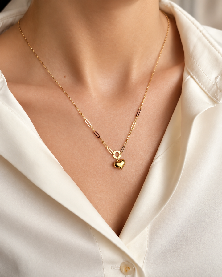 Zarte Halskette aus 18 Karat Gelbgold mit feiner Paperclip-Kette und kleinem Herzanhänger, elegant am Hals getragen, kombiniert mit heller Bluse.