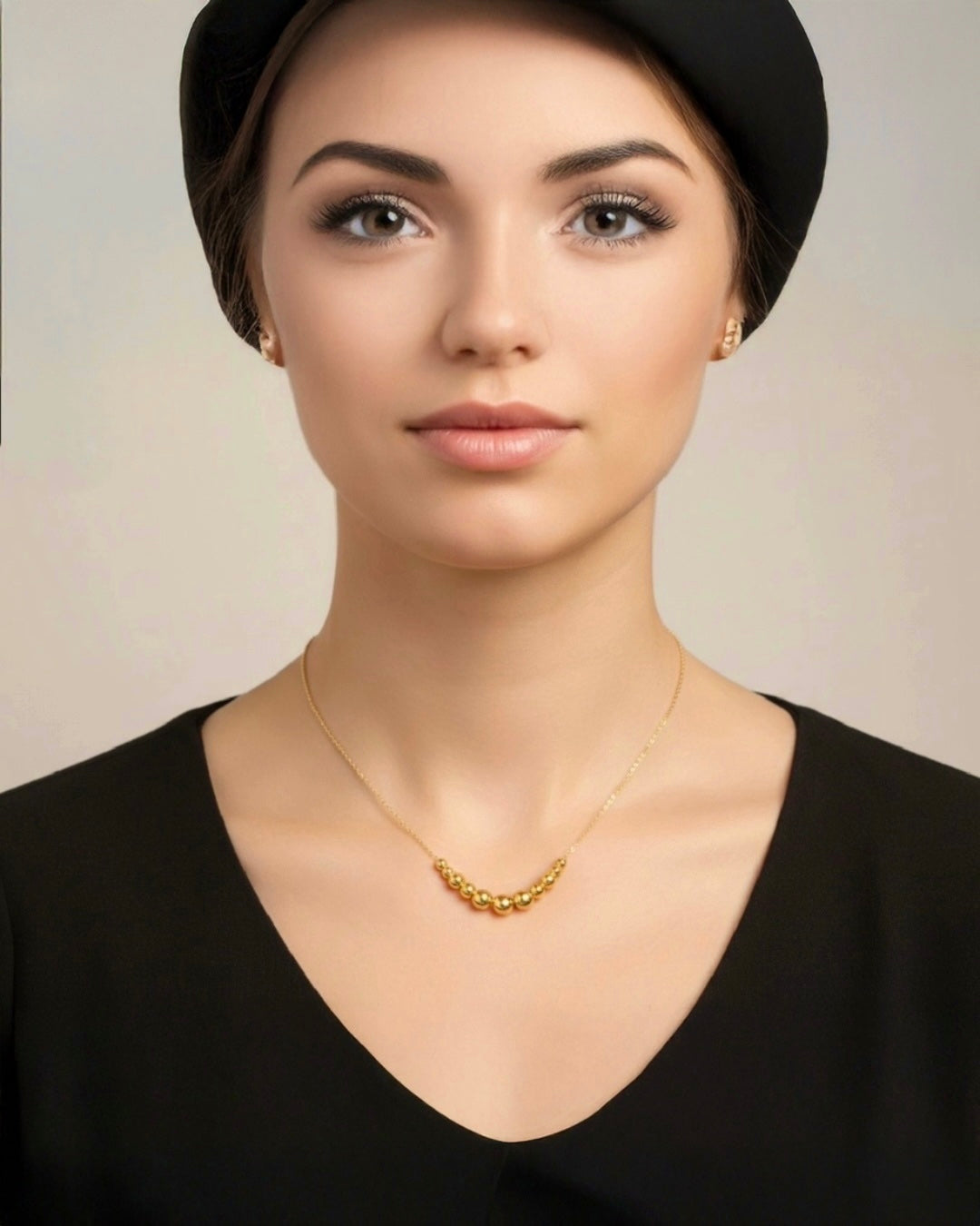 Porträt einer Frau mit eleganter Halskette aus 18k Gelbgold mit kleinen polierten Goldkugeln, minimalistischer luxuriöser Goldschmuck, feine handgefertigte Goldkette.