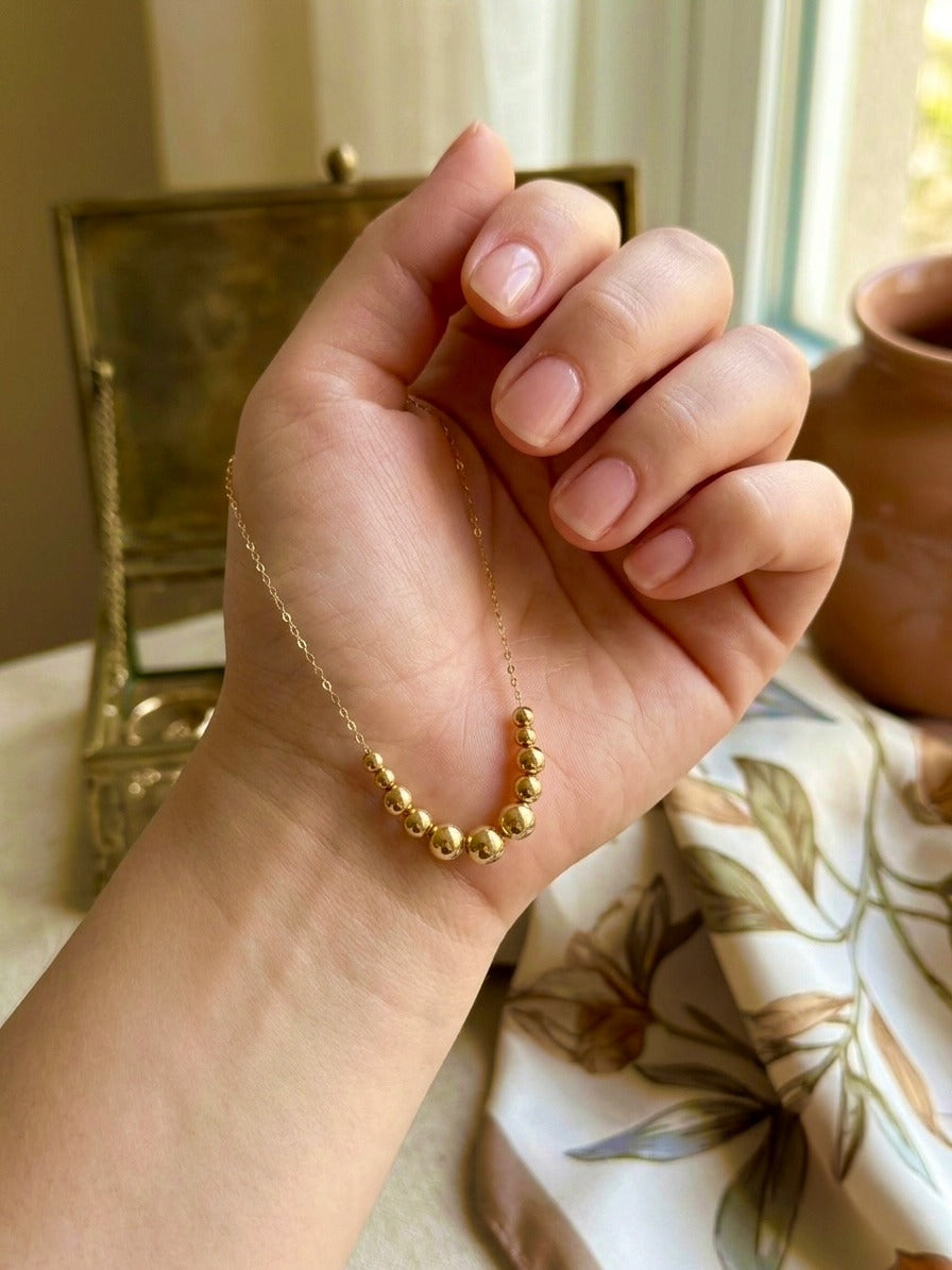 18k Gold Kugelkette mit polierten Goldkugeln in sanftem Farbverlauf, elegant in der Hand gehalten – minimalistischer Goldschmuck für Damen.