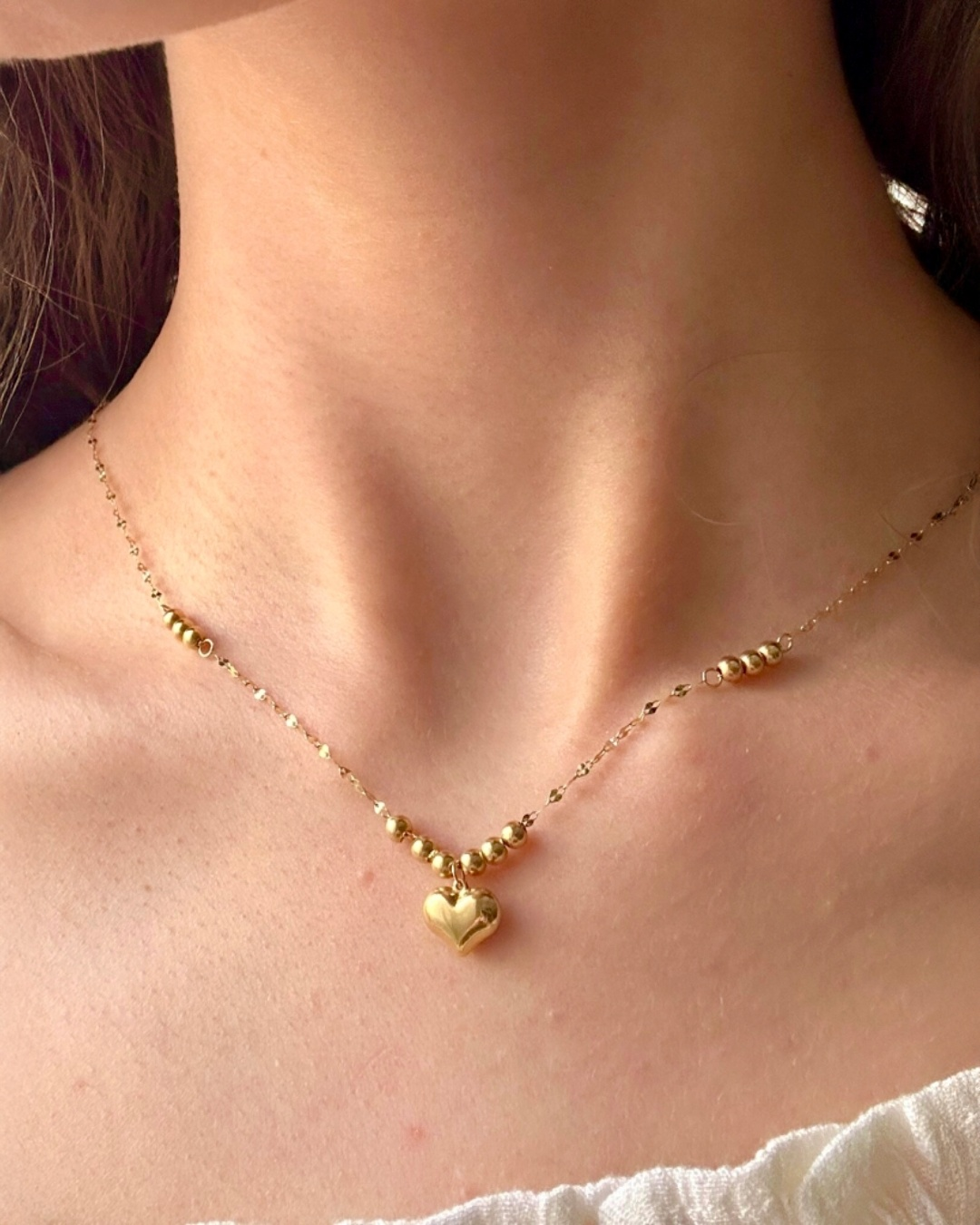 Zarte Damenhalskette aus 18k Gelbgold mit feiner Ankerkette, polierten Goldkugeln und herzförmigem Anhänger, elegant getragen am Hals.