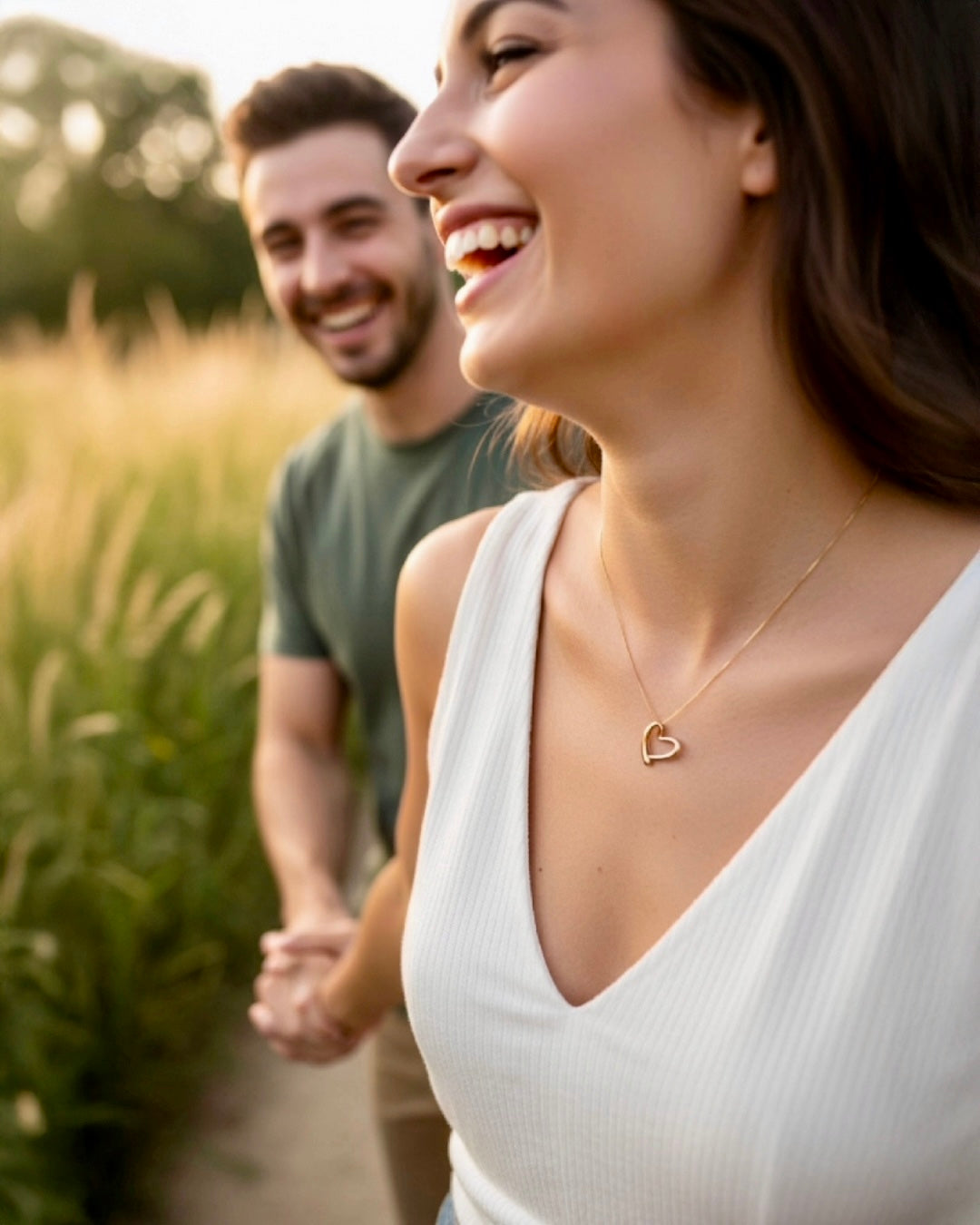 Lachendes Paar bei einem Spaziergang im Grünen, Frau trägt eine feine 18k Gelbgold-Halskette mit Herzanhänger – eleganter, zeitloser Goldschmuck im romantischen Lifestyle-Moment.