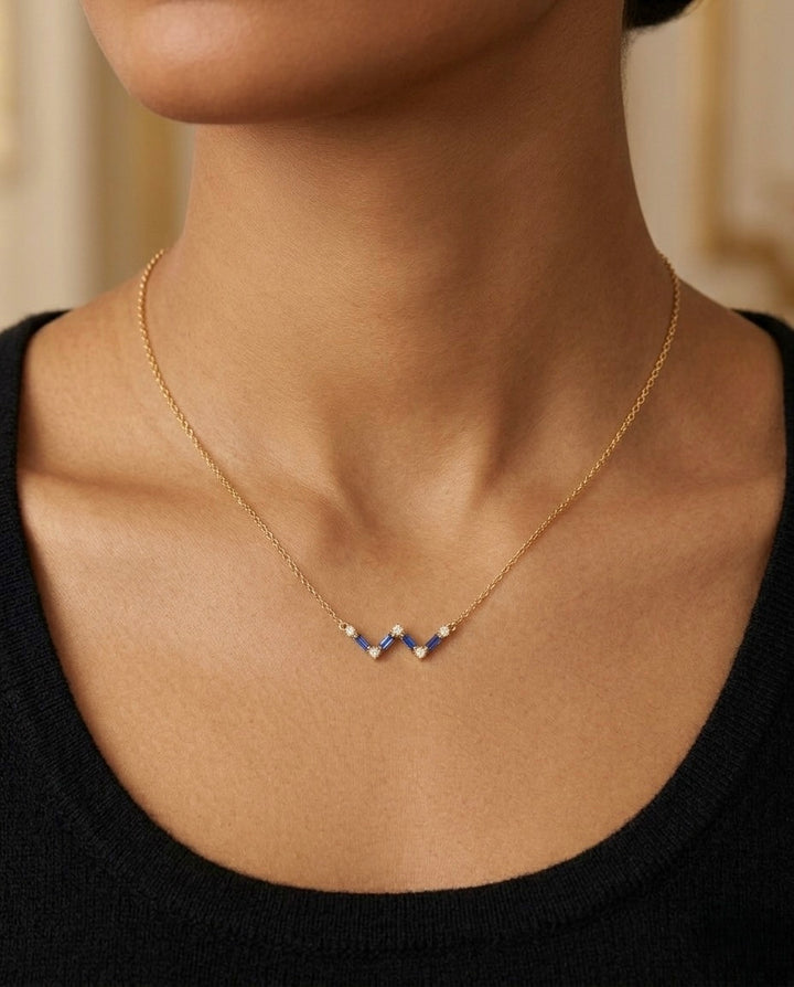 Zarte Halskette aus 18 Karat Gelbgold mit drei tiefblauen Schmuckelementen und funkelnden Zirkonia in V-Form, getragen am Hals einer Frau. Elegantes, minimalistisches Design für Alltag und besondere Anlässe.