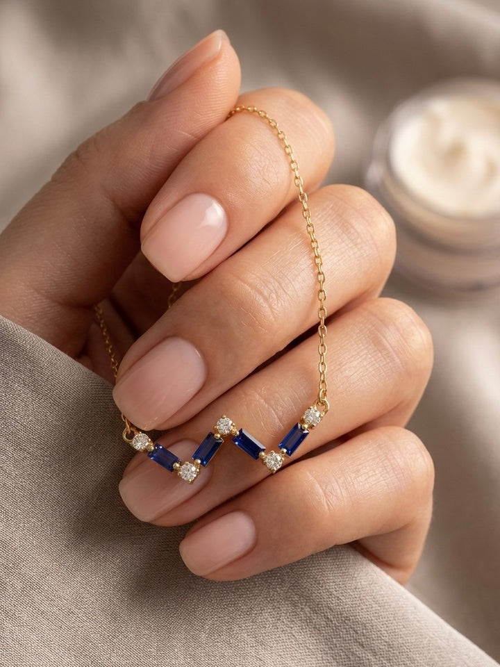 18 Karat Goldhalskette mit blauen Baguette-Saphiren und Diamanten im Zickzack-Design, elegant getragen an einer Hand.