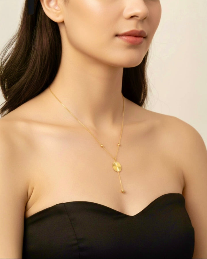 Elegante 18k Gelbgold-Halskette mit ovalem Anhänger und feiner Y-Kette, getragen von einer Frau in schwarzem trägerlosem Kleid