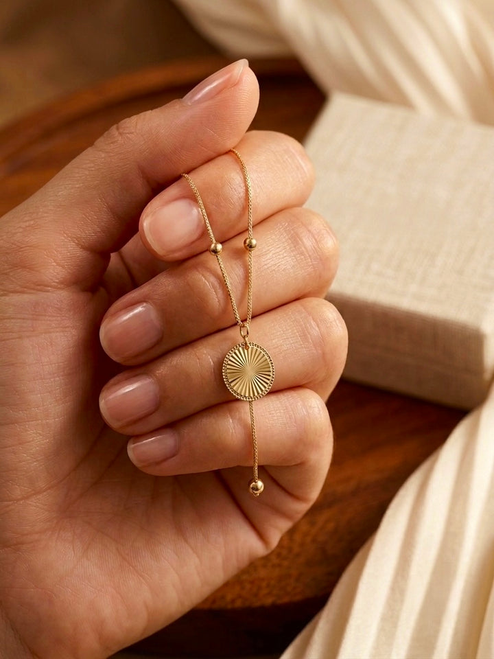 18k Goldarmband mit rundem Sonnenstrahl-Medaillon und verstellbarem Zugverschluss, elegant in einer Hand gehalten