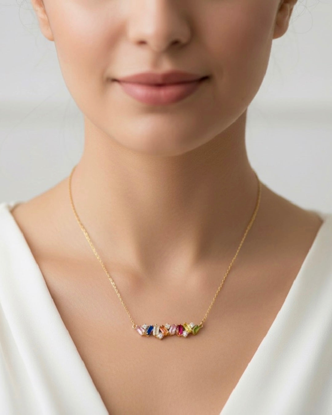 Detailaufnahme einer feinen 18k Gelbgold-Halskette mit farbigen Edelsteinen auf dem Dekolleté, elegant getragen, hochwertiger handgefertigter Goldschmuck für Damen, Ziba Gold.