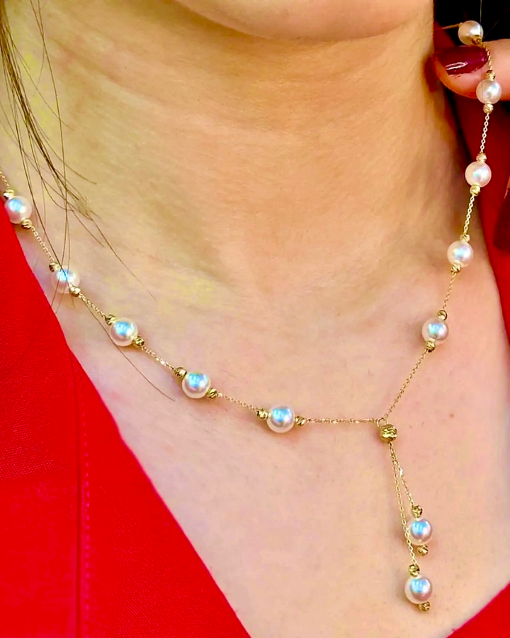 Halskette „Morvarid-e Sefid Raghsan“ aus 18 Karat Gelbgold – feine Kette mit weißen Perlen, die elegant verteilt und im unteren Teil tanzend herabhängen, getragen am Hals über einem roten Outfit.