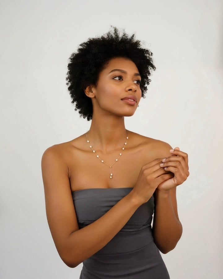 Elegante Frau trägt eine filigrane 18k Goldkette mit feinen Perlen und Y-Anhänger, edler Damenschmuck vor neutralem Hintergrund.