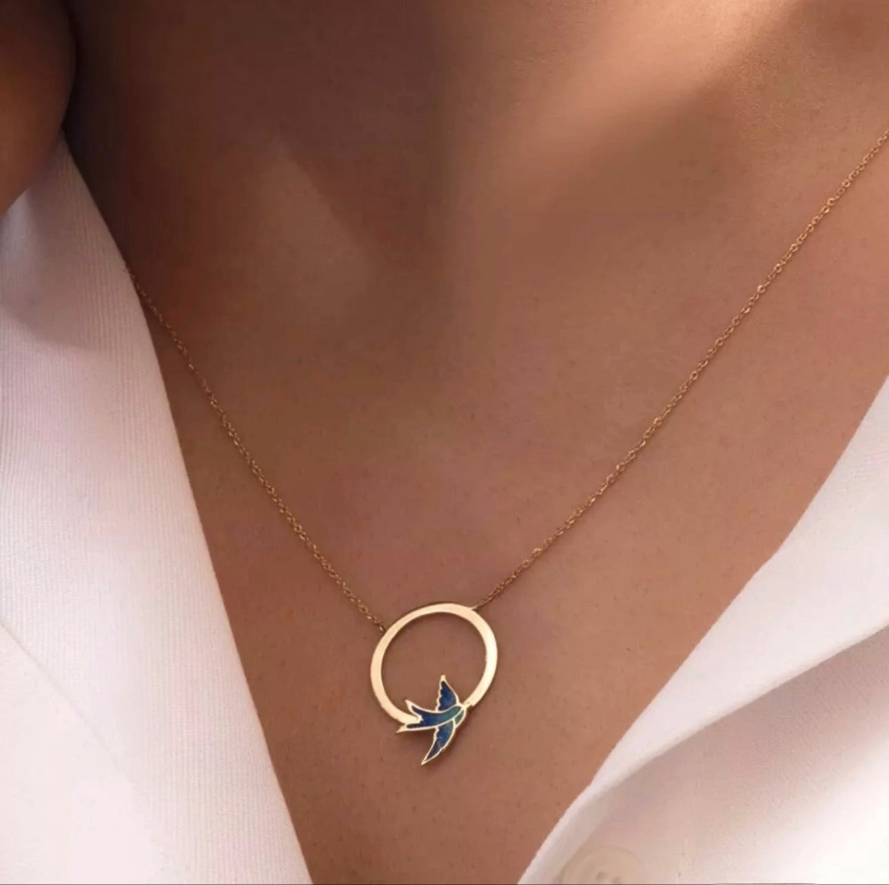 Goldene Halskette mit Ring-Anhänger und fliegender Emaille-Schwalbe – getragen auf der Haut mit weissem Ausschnitt