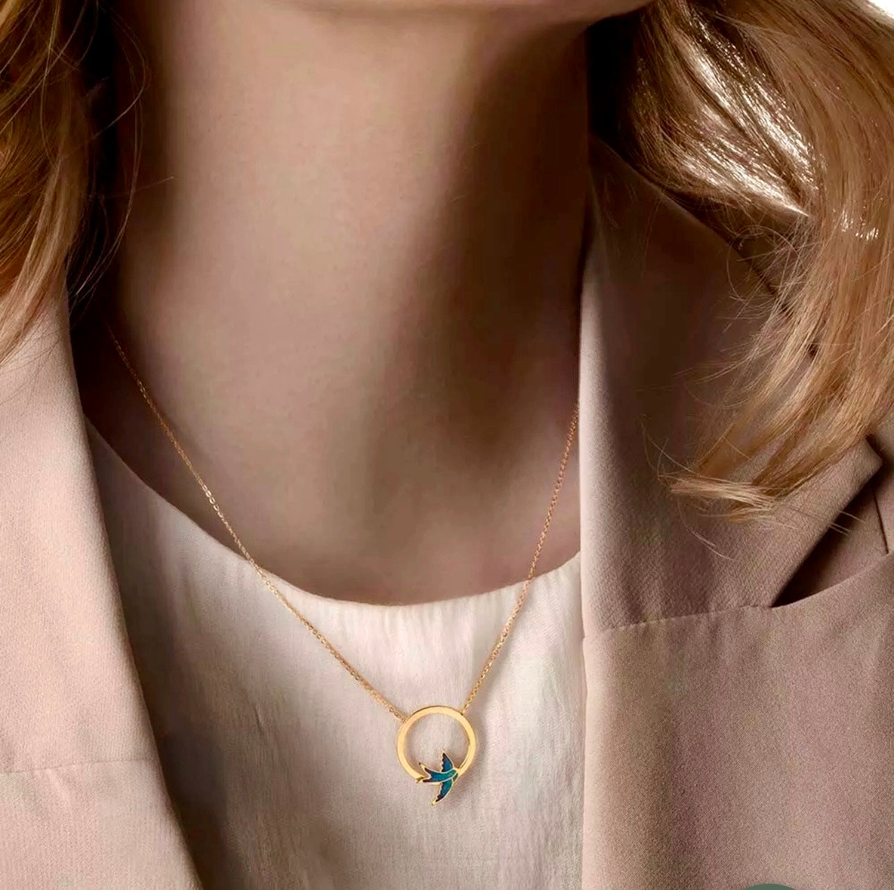 Schmuckstück aus 18k Gold mit runder Form und Schwalbenmotiv – elegant getragen auf hellem Outfit