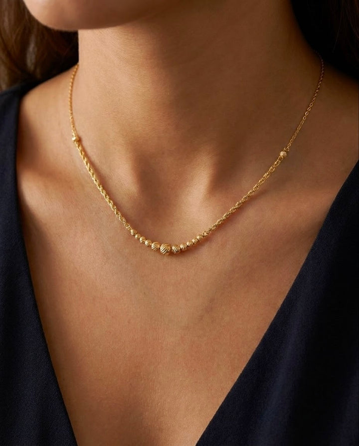18 Karat Goldkette mit feiner Kordelstruktur und strukturierten Goldkügelchen, elegant am Hals getragen.