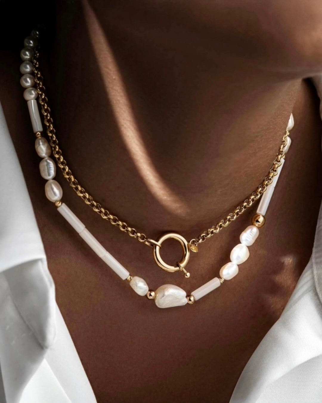 Elegante Halskette aus 18 Karat Gold mit echten weißen Barock-Zuchtperlen, länglichen weißen Perlenelementen und goldenen Akzenten. Das Schmuckstück wird am Hals getragen und kombiniert organische Perlenformen mit modernem Design für einen stilvollen, luxuriösen Look.