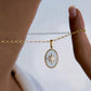 Nahaufnahme einer Halskette aus 18 Karat Gelbgold mit ovalem Anhänger – Perlmuttgrund und ein goldener Stern mit funkelndem Stein in der Mitte, elegant zwischen den Fingern gehalten und vor hellem Hintergrund präsentiert.