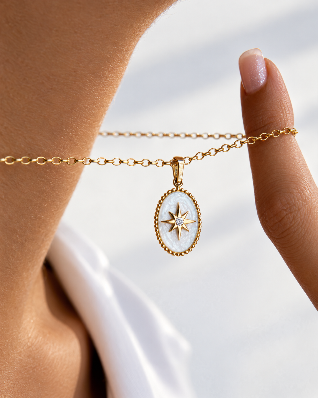 Nahaufnahme einer Halskette aus 18 Karat Gelbgold mit ovalem Anhänger – Perlmuttgrund und ein goldener Stern mit funkelndem Stein in der Mitte, elegant zwischen den Fingern gehalten und vor hellem Hintergrund präsentiert.
