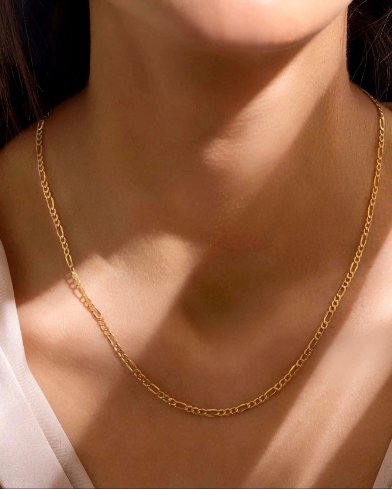 Frau trägt eine schlichte 18k Gelbgold-Halskette im „Salsar“-Design (Barbier), mit filigranen, länglichen Gliedern, die sanft um den Hals liegen und im Sonnenlicht glänzen.