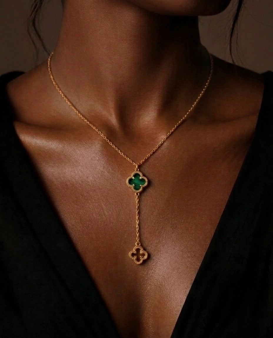 Elegante Y-Halskette aus 18 Karat Gelbgold mit zwei vierblättrigen Kleeblatt-Anhängern. Der obere Anhänger ist mit grünem Malachit besetzt, während der untere als filigranes Goldmotiv gestaltet ist. Die luxuriöse Halskette wird an einem Model vor schwarzer Kleidung präsentiert und verbindet zeitlose Eleganz mit modernem Design – ideal als exklusiver Goldschmuck für Damen.