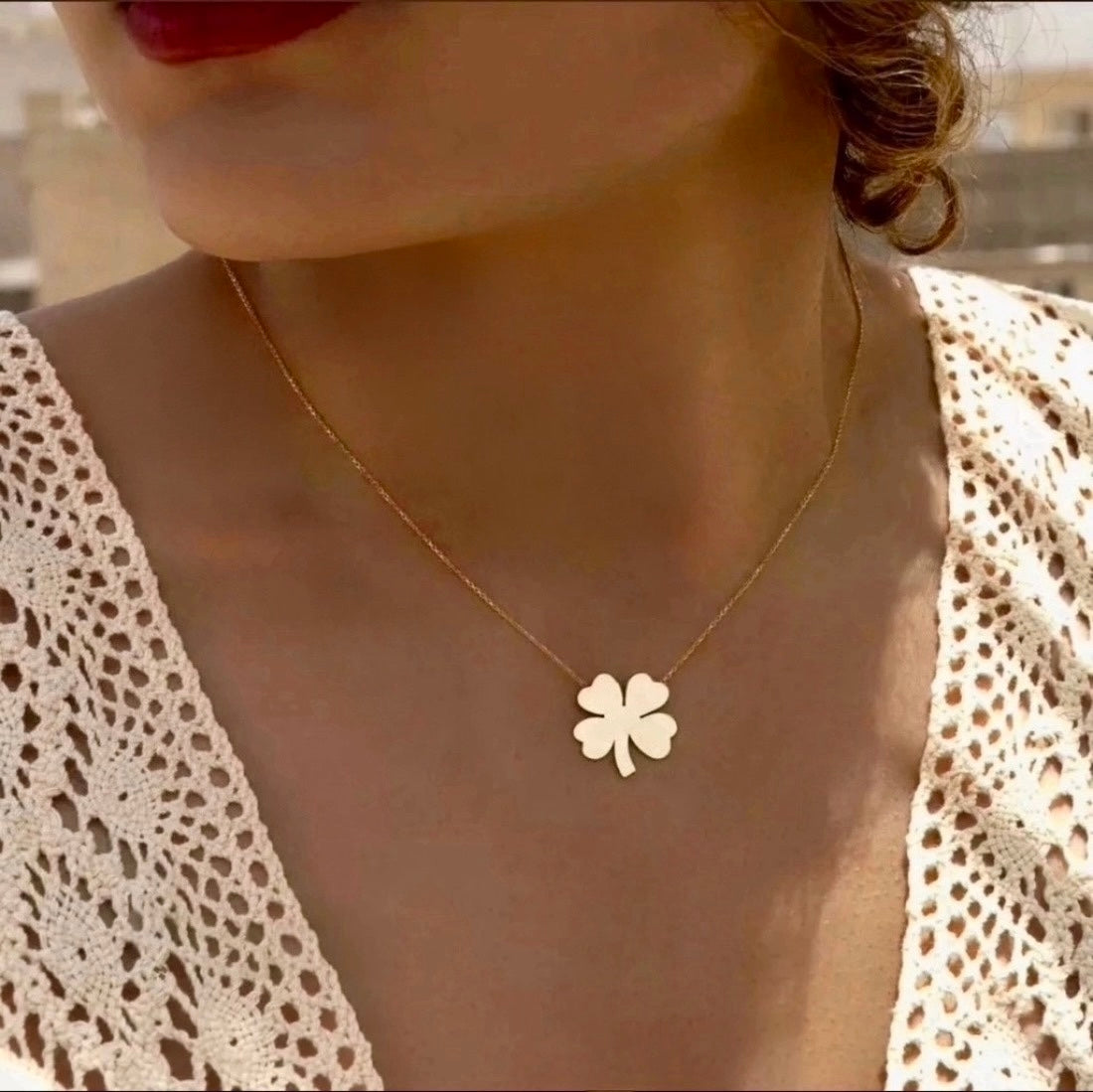 Feine Halskette aus 18k Gelbgold mit einem filigranen Anhänger in Form eines vierblättrigen Kleeblatts, getragen von einer Frau in gehäkelter Spitzenbluse.