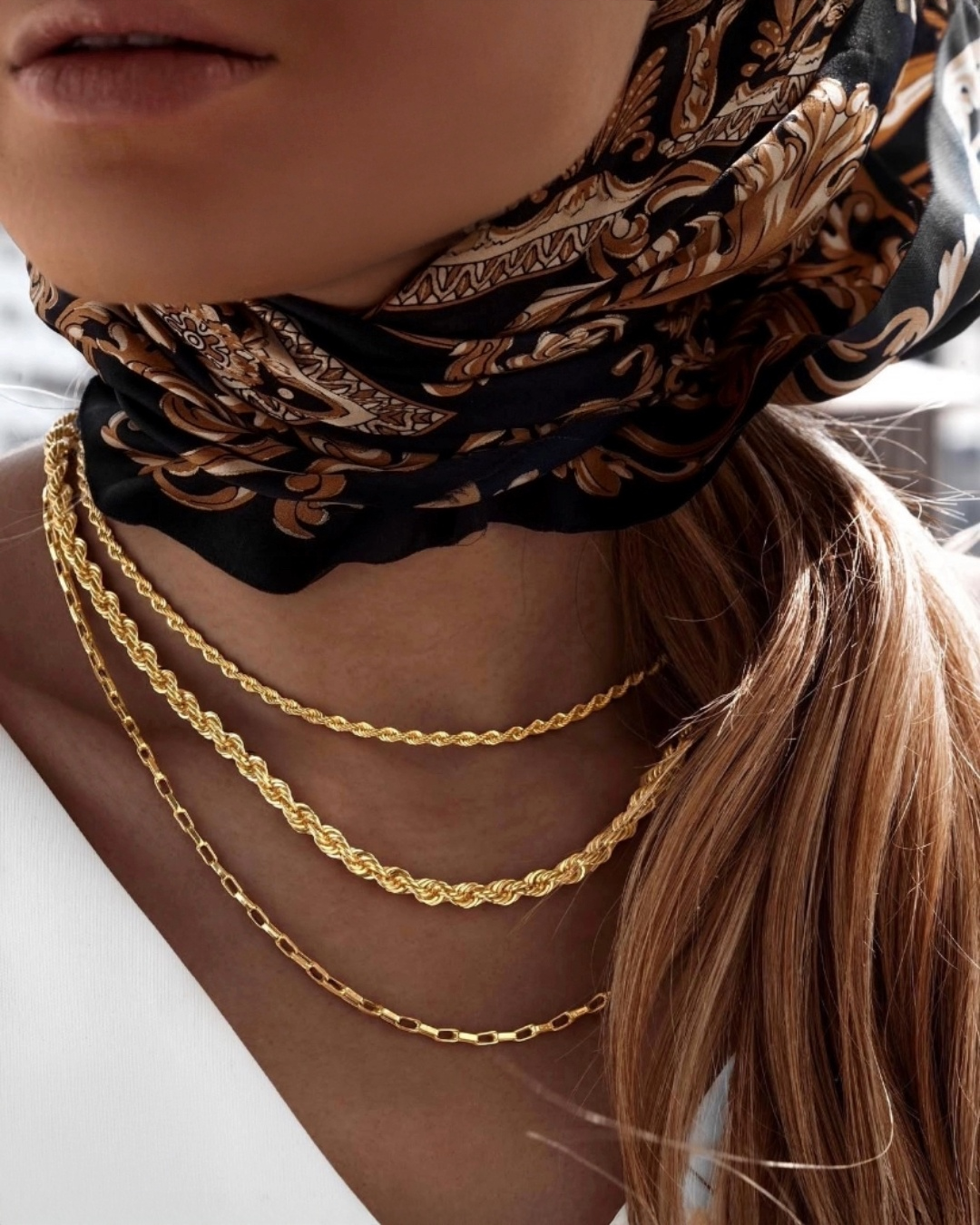 Layering aus 18 Karat Gelbgold-Halsketten mit Kordel- und Figarokette, elegant getragen am Hals, kombiniert mit Seidentuch – zeitloser Goldschmuck von Ziba Gold.