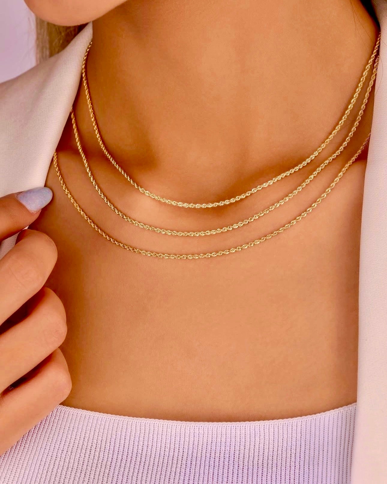 Nahaufnahme eines Halses mit drei filigranen 18k Gelbgold-Kordelketten in unterschiedlichen Längen, übereinander getragen, kombiniert mit einem weißen Blazer und einem hellen Stricktop.