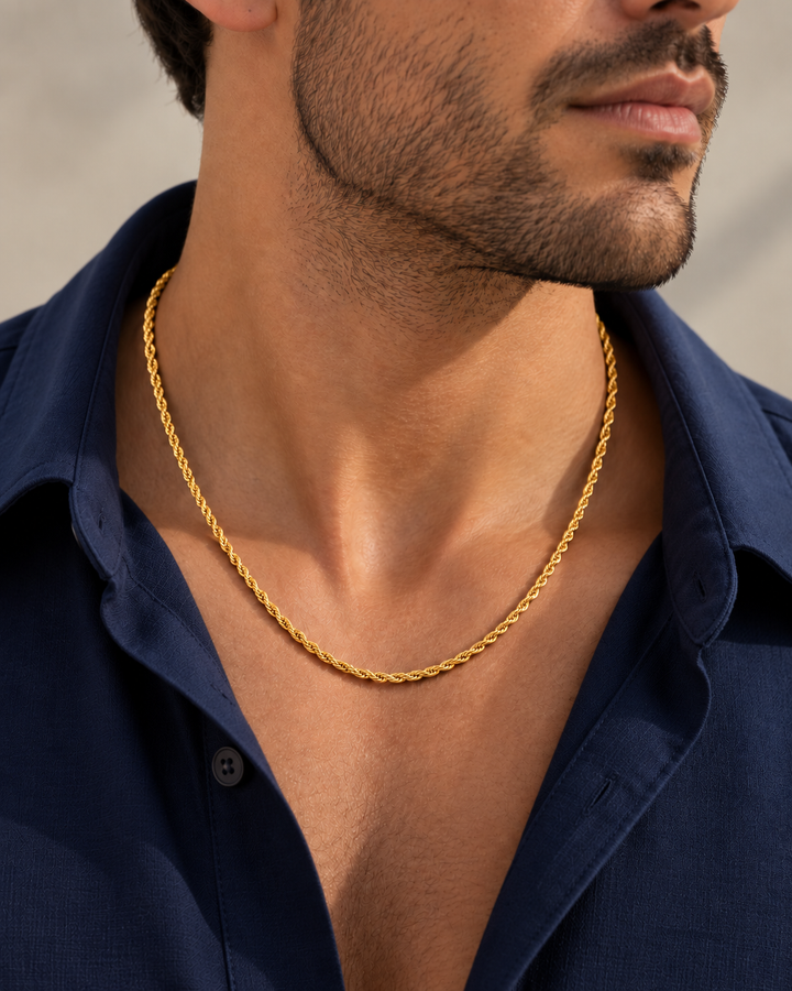 Nahaufnahme eines Mannes mit feiner gedrehter Seilkette aus Gelbgold, elegant getragen zu einem blauen Hemd.
