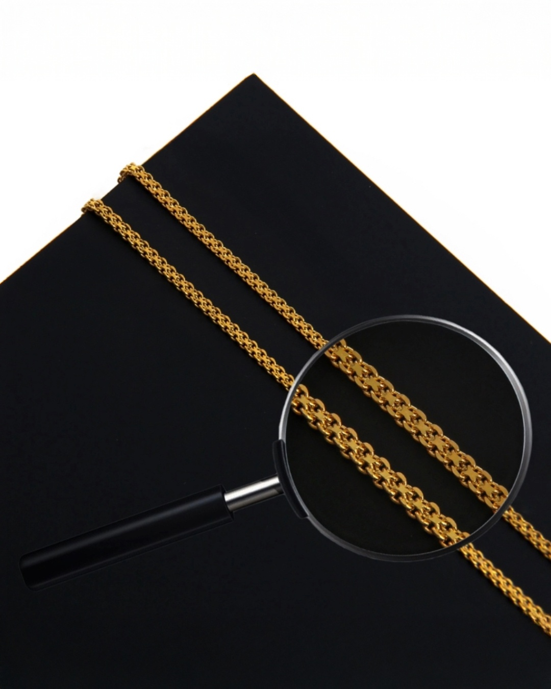 Detailaufnahme einer glänzenden 18k-Goldkette, die auf schwarzem Hintergrund liegt. Eine Lupe vergrößert einen Abschnitt der kunstvoll gearbeiteten, dicht verwobenen Gliederkette und zeigt die feine Struktur im Close-up.