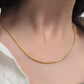 Nahaufnahme eines Halses mit einer feinen, gleichmäßig gearbeiteten 18k-Goldkette. Die Kette liegt elegant am Schlüsselbein an, wirkt glatt, glänzend und dezent. Der Hintergrund zeigt neutrale Kleidung, wodurch das Gold stärker hervortritt.
