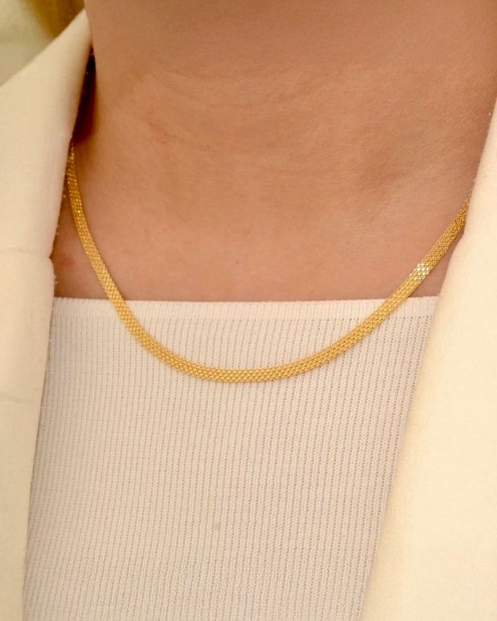 18k Gelbgold-Halskette in feiner Fischgrätenoptik, elegant am Hals getragen, kombiniert mit hellem Top und Blazer – zeitloser, minimalistischer Goldschmuck.