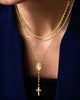 Mehrlagige 18k Goldkette, bestehend aus feinen Gliederketten und einer längeren Rosenkranzkette mit ovalem Medaillon und Kreuzanhänger, getragen über einem dunklen Top und Blazer.