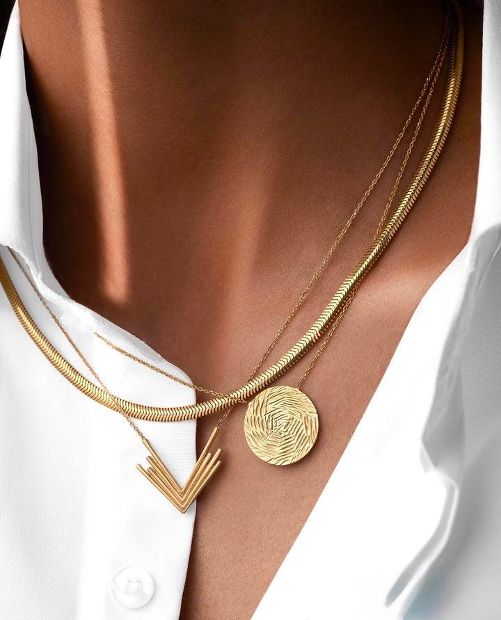 Mehrere elegante Halsketten aus Gelbgold mit rundem Anhänger und geometrischem Anhänger, stilvoll kombiniert auf weisser Bluse.
