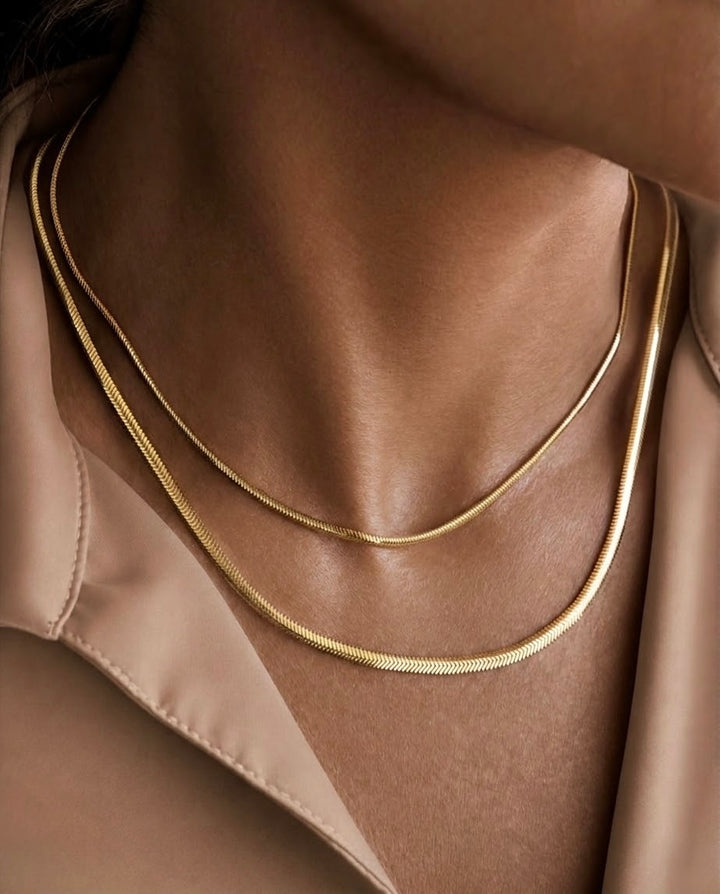 Zwei feine Halsketten aus 18k Gelbgold in unterschiedlichen Stärken, elegant im Layering getragen am Dekolleté einer Frau.