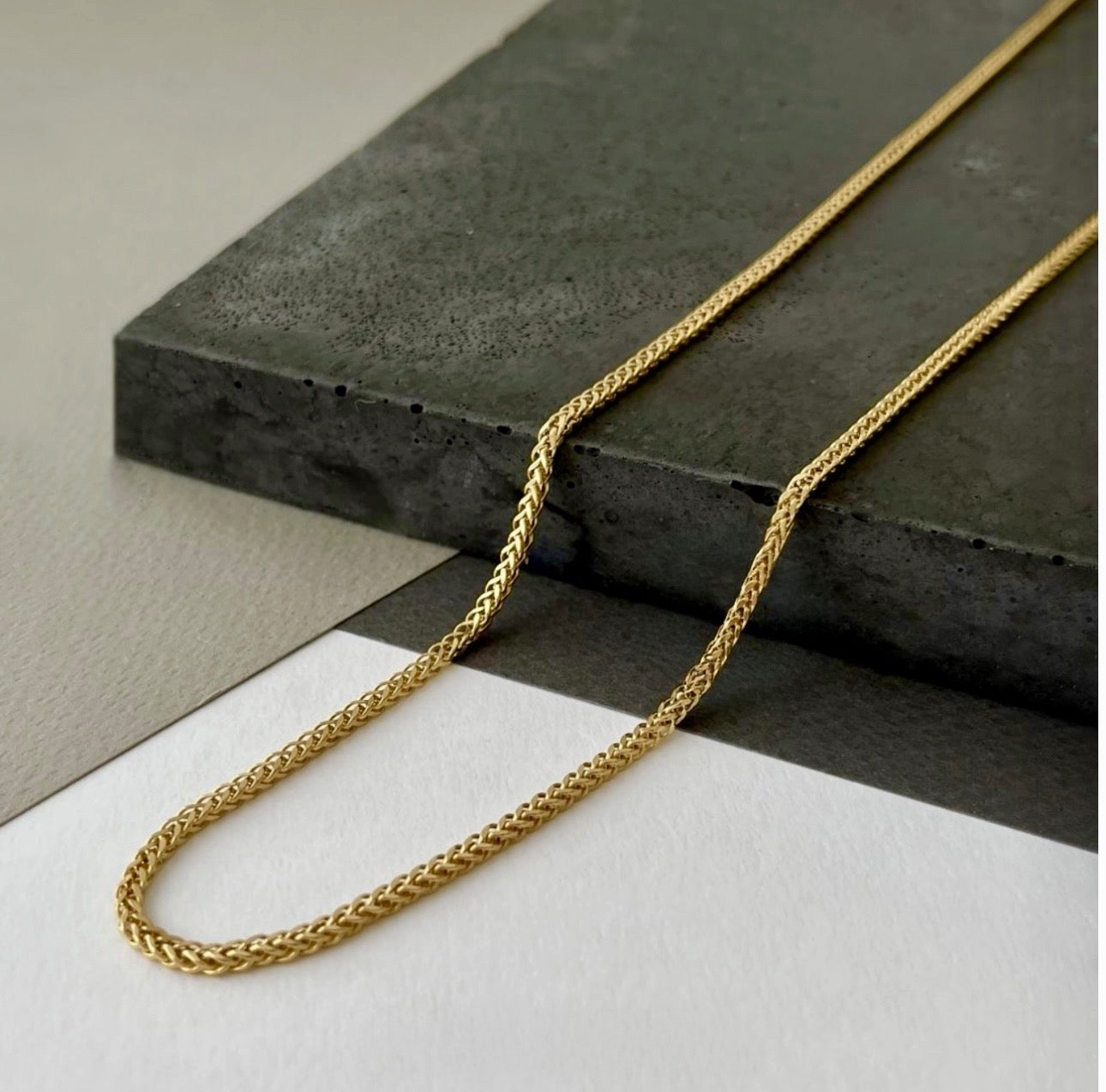 Zopfmuster-Halskette aus 18k Gelbgold mit 3 mm breiten Gliedern – elegant drapiert auf schwarzer Steinplatte