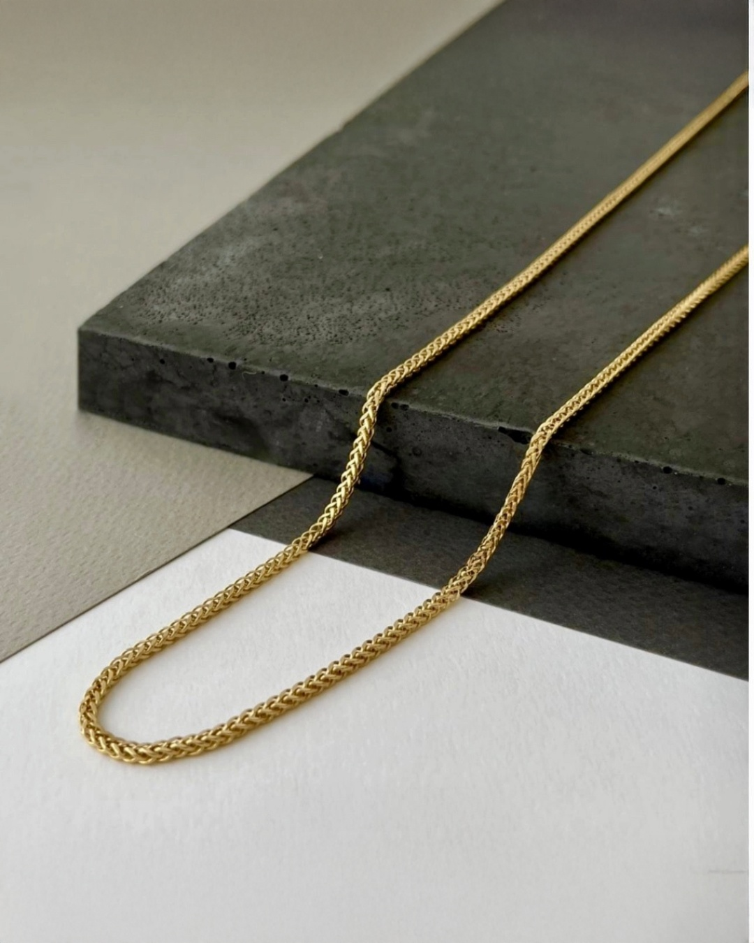 Zopfmuster-Halskette aus 18k Gelbgold mit 3 mm breiten Gliedern – elegant drapiert auf schwarzer Steinplatte