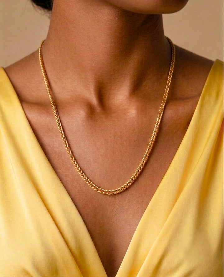 Nahaufnahme einer Person mit einer eleganten 18-karätigen Gelbgold-Halskette im Schlangenketten-Design. Die feingliedrige, glänzende Kette liegt geschmeidig am Hals und reflektiert das warme Licht dezent. Getragen wird sie zu einem gelben V-Ausschnitt-Kleid, dessen Farbton das Gold harmonisch ergänzt. Der ruhige, neutrale Hintergrund lenkt den Fokus vollständig auf den hochwertigen Goldschmuck und seine zeitlose Eleganz.
