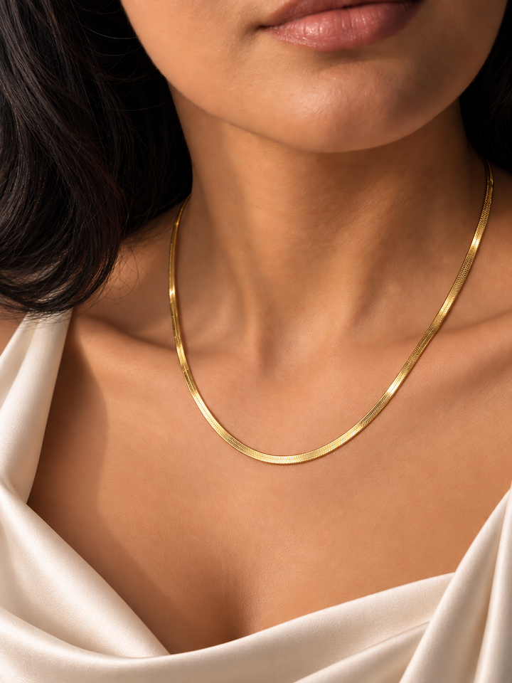 Elegante Frau trägt eine flache Halskette aus 18 Karat Gelbgold zu einem edlen cremefarbenen Satinkleid.
