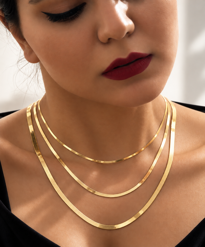 Elegante Frau mit drei unterschiedlich langen Halsketten aus 18 Karat Gelbgold und passendem Ohrschmuck im luxuriösen Fashion-Look.