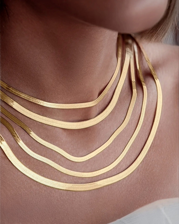 Mehrere übereinander getragene Fischgrätenketten aus 18k Gelbgold in unterschiedlichen Breiten, elegant am Hals drapiert und mit seidigem Glanz.