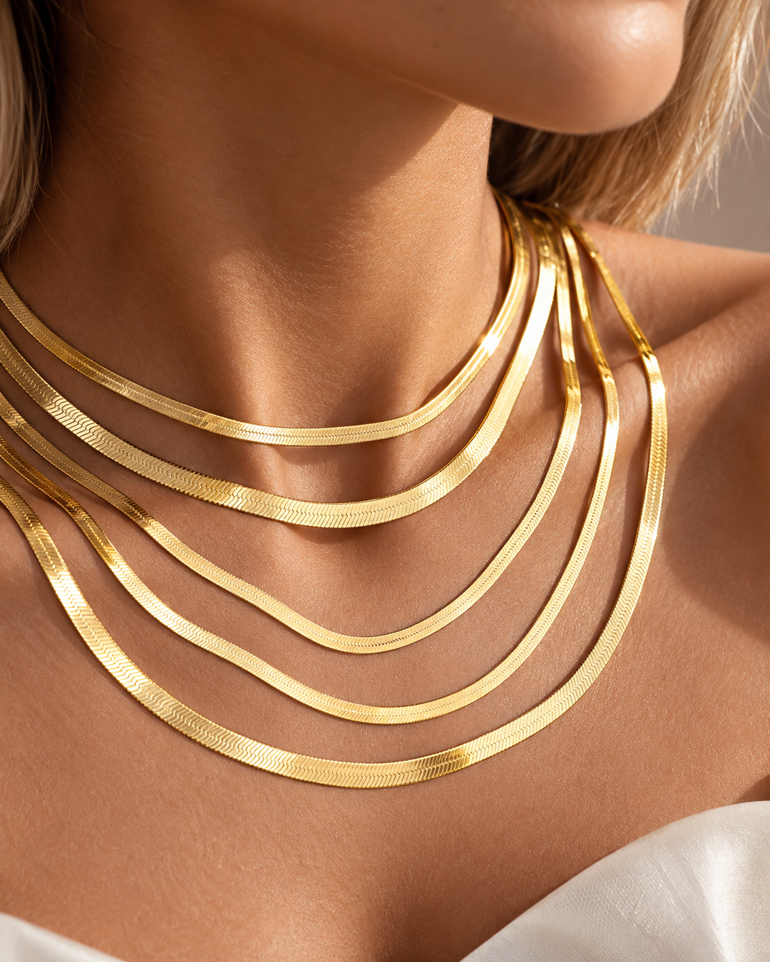 Mehrere übereinander getragene Fischgrätenketten aus 18k Gelbgold in unterschiedlichen Breiten, elegant am Hals drapiert und mit seidigem Glanz.