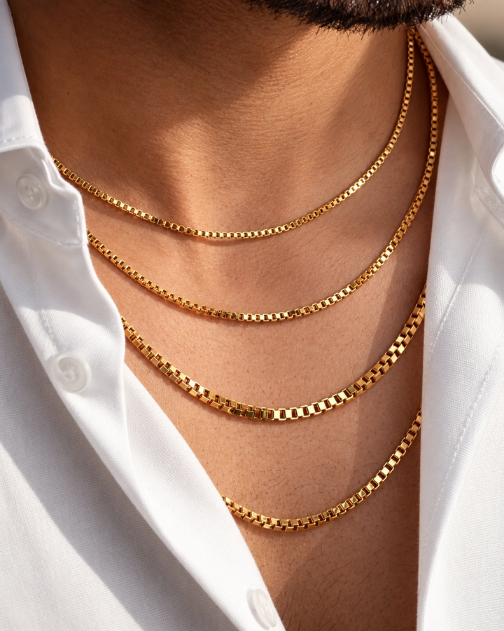Mehrlagig getragene 18k Gelbgold-Halsketten mit eckiger Gliederstruktur (Box Chain) an einem männlichen Hals, kombiniert mit offenem weissen Hemd – minimalistischer, eleganter Goldschmuck mit modernem Layering-Look.