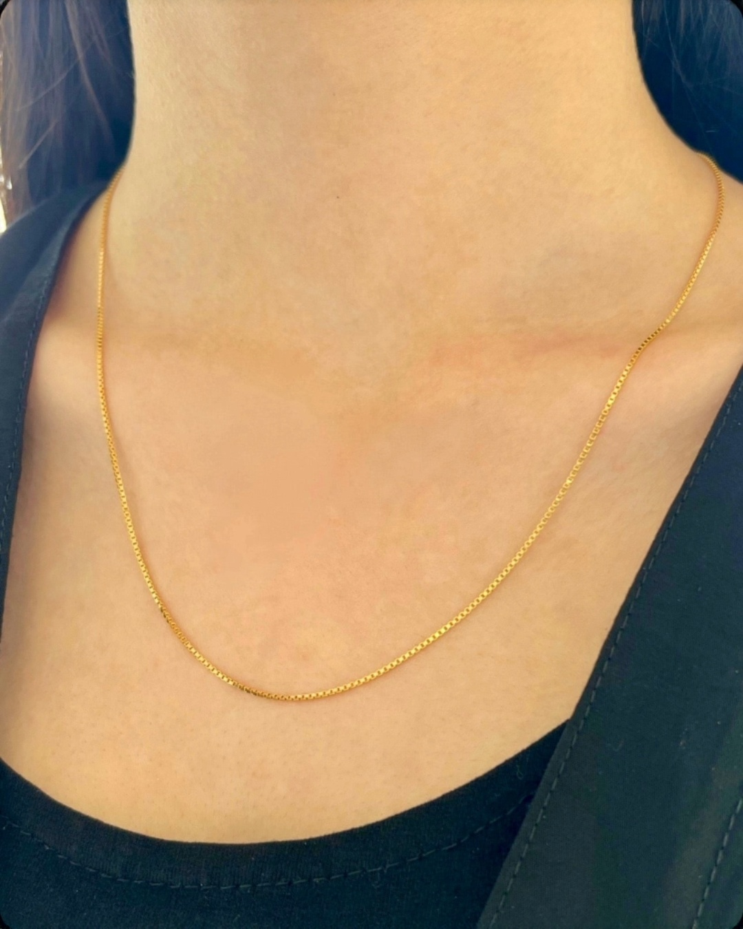 Feine 18k Gelbgold-Halskette mit dezenter, eckiger Gliederstruktur (Box Chain), elegant am Hals getragen, kombiniert mit schwarzem Oberteil – minimalistischer, zeitloser Goldschmuck für den Alltag und besondere Anlässe.