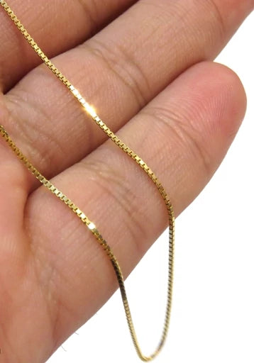 Nahaufnahme einer Venedig-Kette aus 18k Gelbgold, locker über die Finger einer Hand gelegt. Die feinen, quadratisch geschnittenen Glieder reflektieren das Licht gleichmäßig und erzeugen einen klaren, präzisen Glanz. Hintergrund neutral und unscharf.