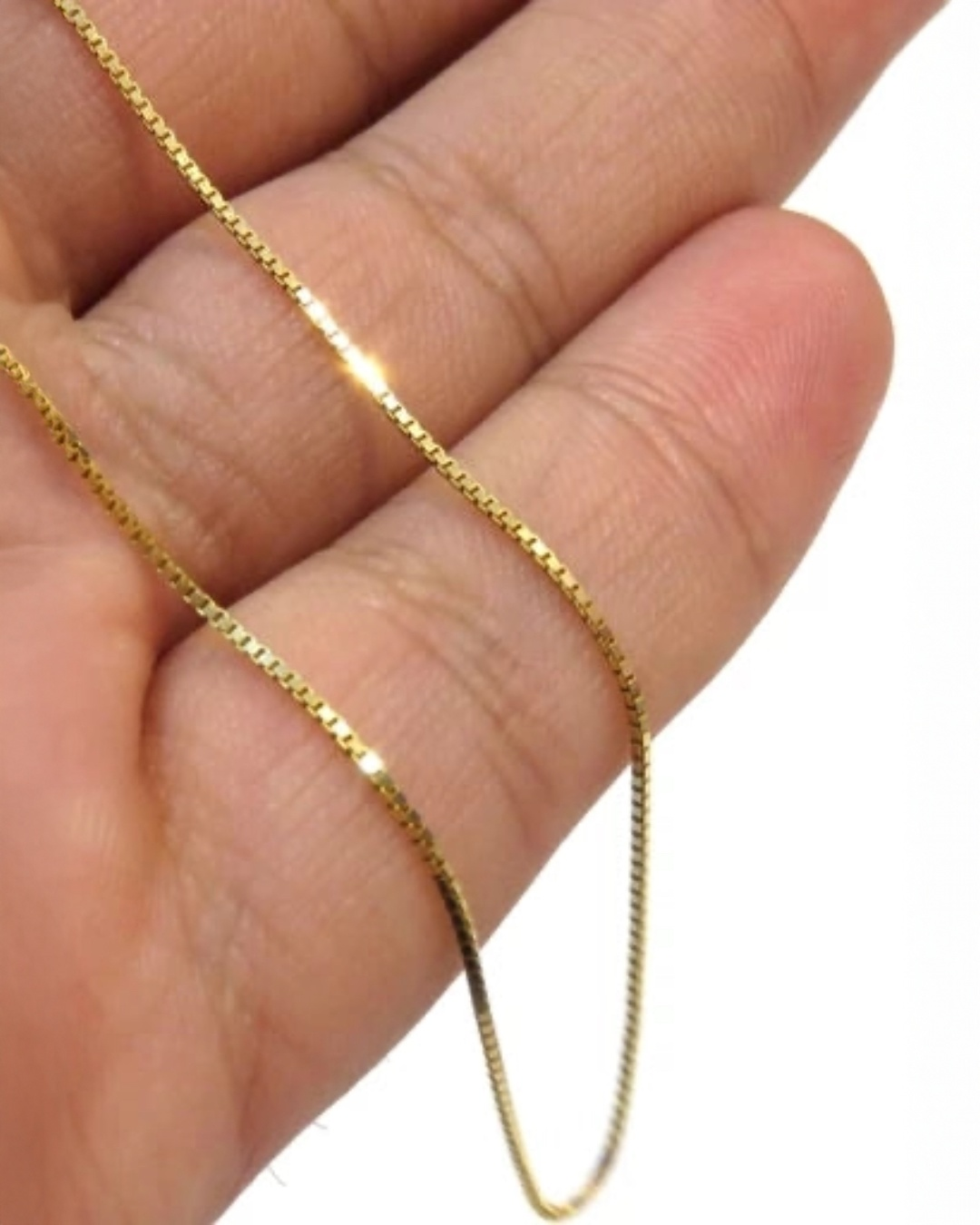 Nahaufnahme einer Venedig-Kette aus 18k Gelbgold, locker über die Finger einer Hand gelegt. Die feinen, quadratisch geschnittenen Glieder reflektieren das Licht gleichmäßig und erzeugen einen klaren, präzisen Glanz. Hintergrund neutral und unscharf.