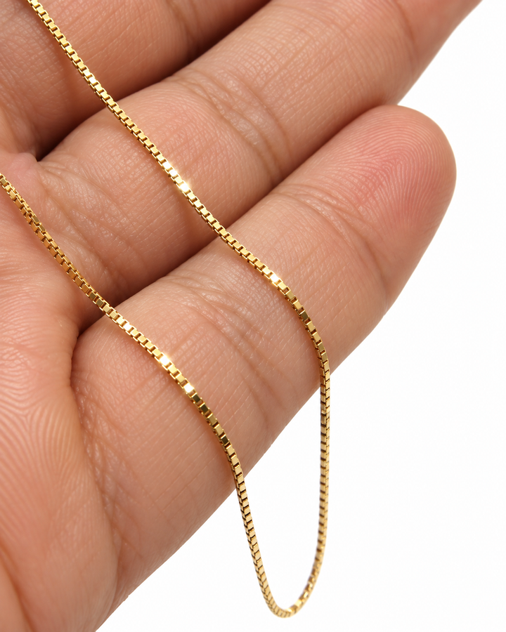 Nahaufnahme einer Venedig-Kette aus 18k Gelbgold, locker über die Finger einer Hand gelegt. Die feinen, quadratisch geschnittenen Glieder reflektieren das Licht gleichmäßig und erzeugen einen klaren, präzisen Glanz. Hintergrund neutral und unscharf.