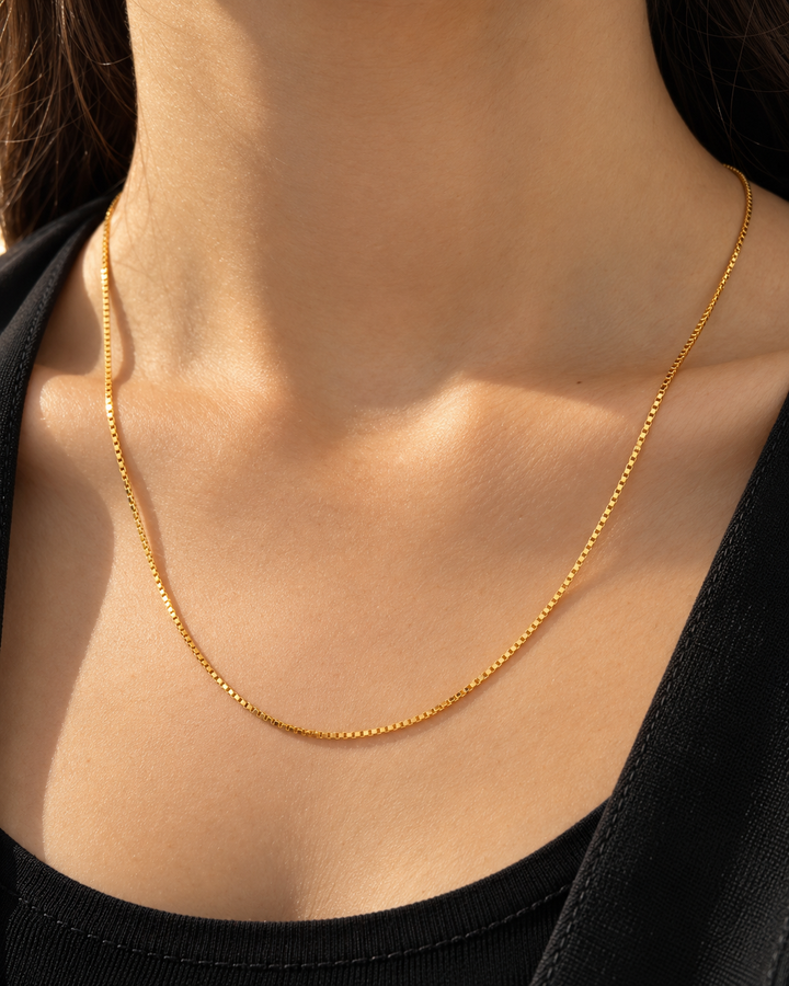 Feine 18k Gelbgold-Halskette mit dezenter, eckiger Gliederstruktur (Box Chain), elegant am Hals getragen, kombiniert mit schwarzem Oberteil – minimalistischer, zeitloser Goldschmuck für den Alltag und besondere Anlässe.
