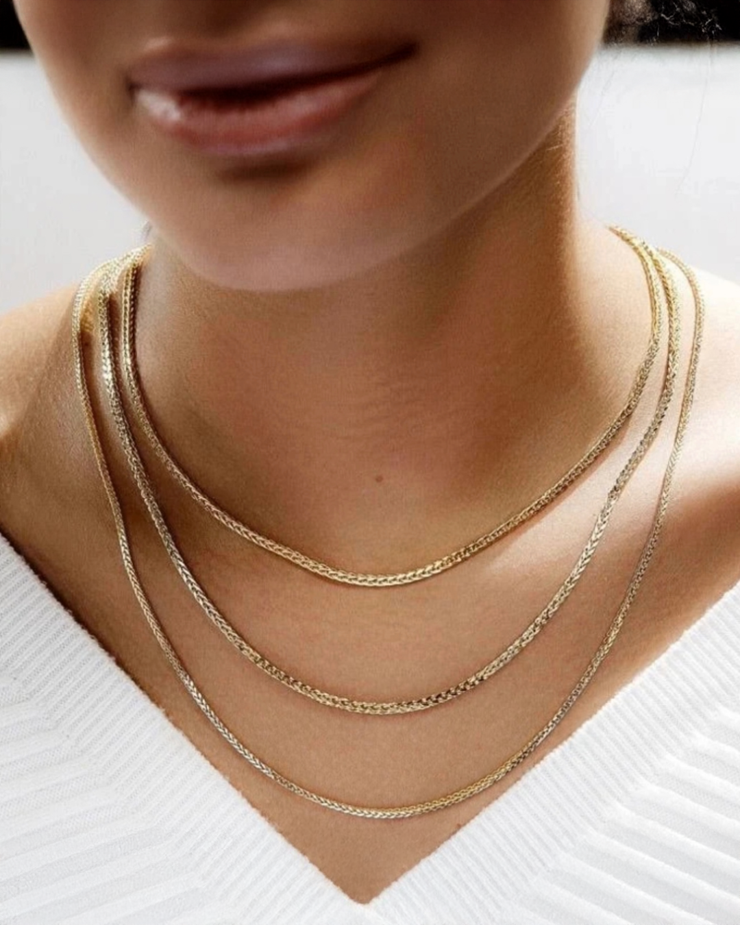 Mehrlagige Halskette aus 18 K Gelbgold, filigrane Ketten in verschiedenen Längen elegant übereinander getragen, edler Goldschmuck am Hals einer Frau vor hellem Hintergrund.