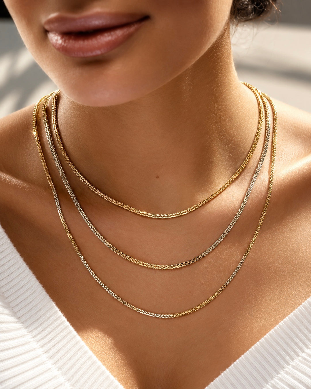 Mehrlagige Halskette aus 18 K Gelbgold, filigrane Ketten in verschiedenen Längen elegant übereinander getragen, edler Goldschmuck am Hals einer Frau vor hellem Hintergrund.